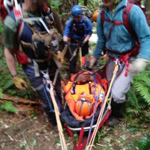 This image presents, a rope rescue ops team performing patient packaging and litter attending in a low angle environment while using the principles of ascending lines with mechanical advantage systems and anchor systems, to promote Crux Rescue's training course product, Rescue Rope Ops.