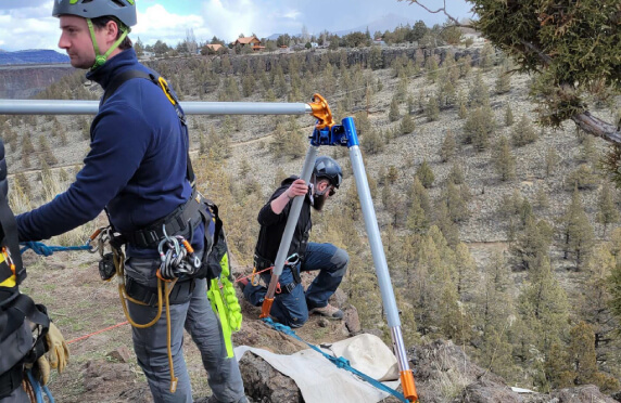 Image presents the picture of a rope rescue team with a tripod at the edge of a canyon as a pictorial for the Crux Rescue ProQual assessment tests, available to rope rescue pros, to determine their level of skill competency and mastery.